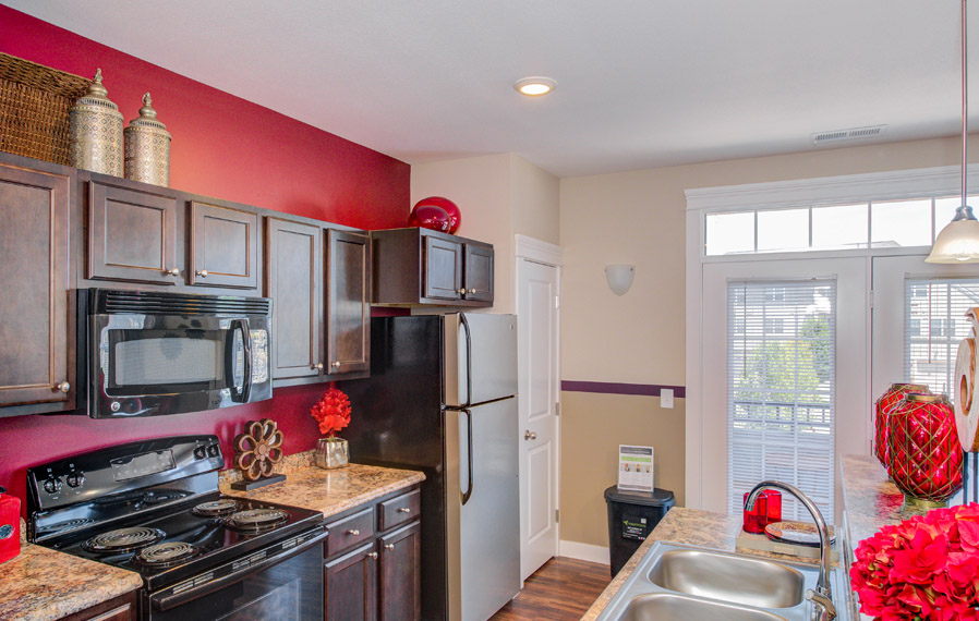 A dark cabinet kitchen with red walls facing the oven and sink.